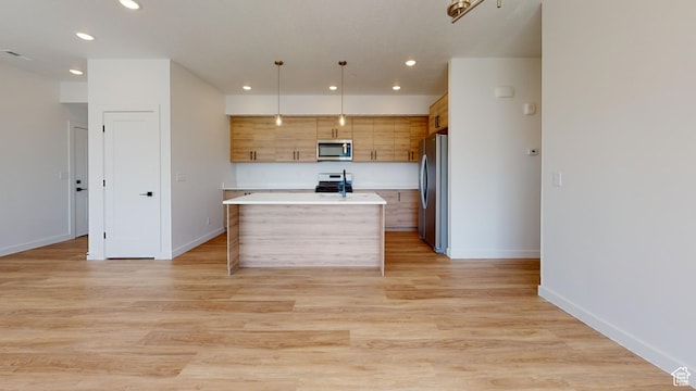kitchen featuring hanging light fixtures, light wood-type flooring, appliances with stainless steel finishes, and a center island with sink