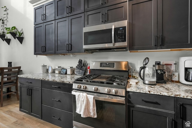 kitchen with appliances with stainless steel finishes, light hardwood / wood-style flooring, and light stone countertops