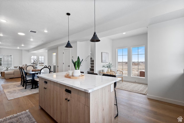kitchen featuring pendant lighting, a kitchen island, hardwood / wood-style flooring, light stone countertops, and a breakfast bar area