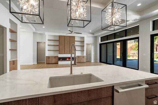 kitchen with hanging light fixtures, built in shelves, stainless steel dishwasher, a fireplace, and sink