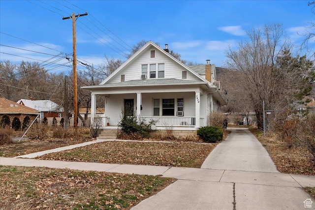 bungalow-style home featuring a chimney, driveway, a porch, and fence