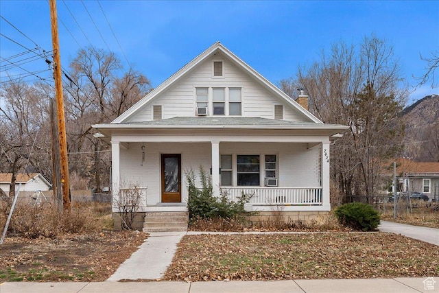 bungalow featuring a chimney, brick siding, and covered porch