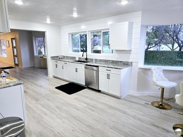 kitchen with light wood-style flooring, white cabinets, a sink, light stone countertops, and dishwasher