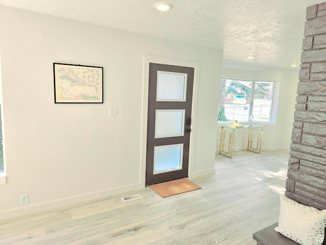 entrance foyer with baseboards, visible vents, a textured ceiling, and light wood finished floors