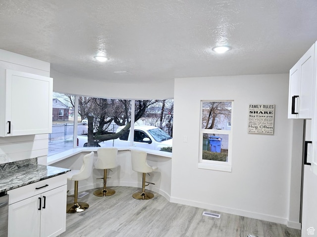 kitchen featuring light wood-style floors, white cabinets, visible vents, and a textured ceiling