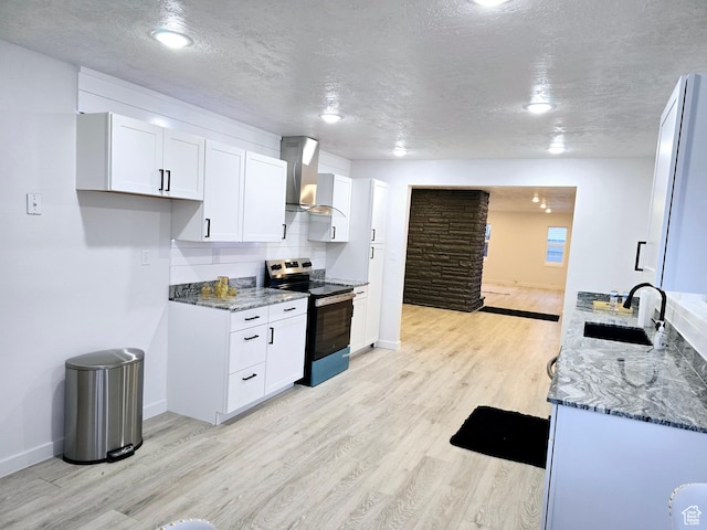 kitchen featuring stainless steel electric stove, light wood-style floors, a sink, dark stone counters, and wall chimney exhaust hood