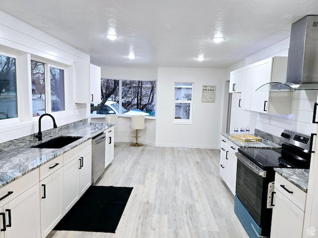 kitchen with light wood-style flooring, electric range oven, a sink, dishwasher, and wall chimney exhaust hood