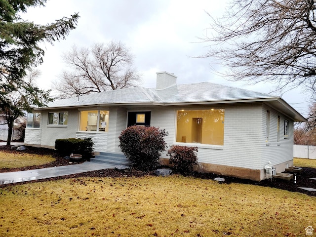 single story home featuring brick siding, a chimney, and a front yard