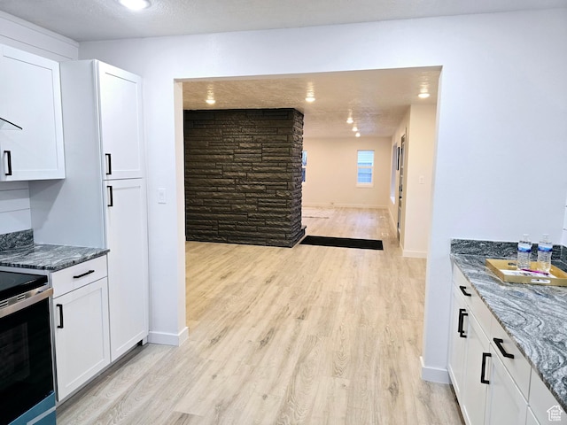 kitchen with white cabinetry, baseboards, light wood-style floors, dark stone countertops, and stainless steel range with electric stovetop