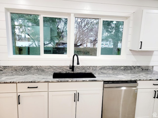 kitchen featuring stainless steel dishwasher, a sink, a wealth of natural light, and white cabinets