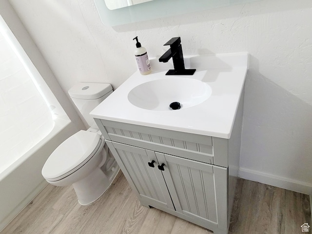 full bath featuring a tub to relax in, vanity, toilet, and wood finished floors