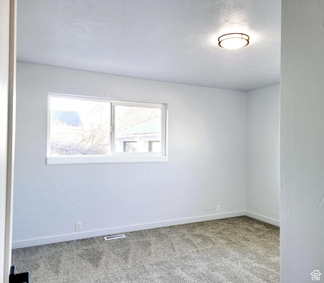 unfurnished room with a textured ceiling, carpet flooring, visible vents, and baseboards