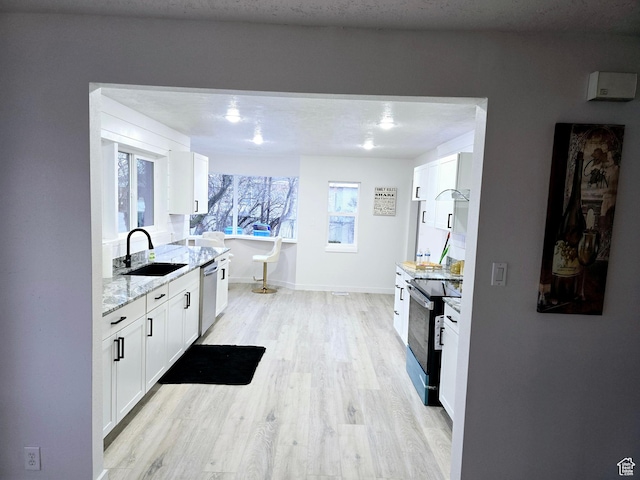 kitchen featuring light wood finished floors, dishwasher, black range with electric cooktop, white cabinetry, and a sink
