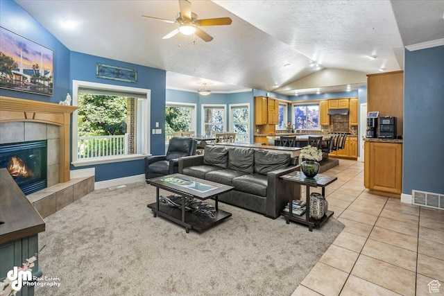 tiled living room with ceiling fan, vaulted ceiling, a tiled fireplace, and a textured ceiling