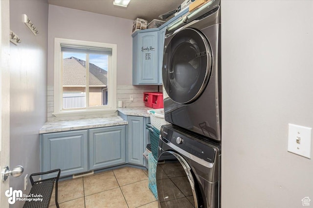 laundry room with stacked washing maching and dryer, cabinets, and light tile patterned floors
