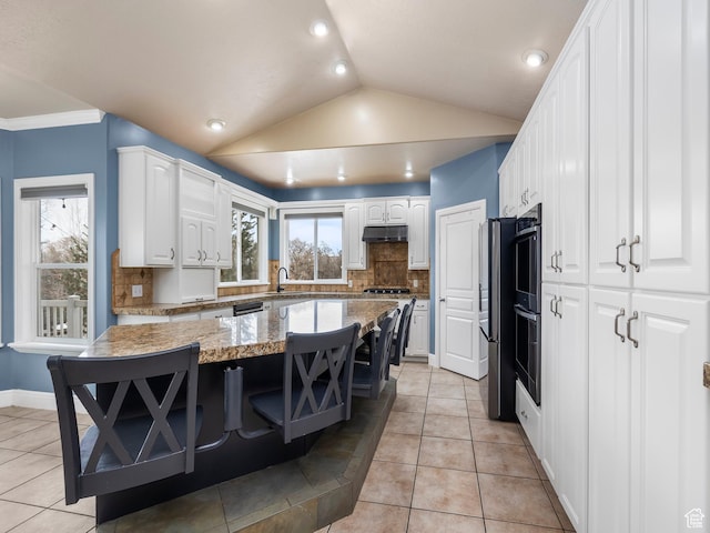 kitchen with white cabinetry, lofted ceiling, a kitchen island, stone countertops, and light tile patterned flooring
