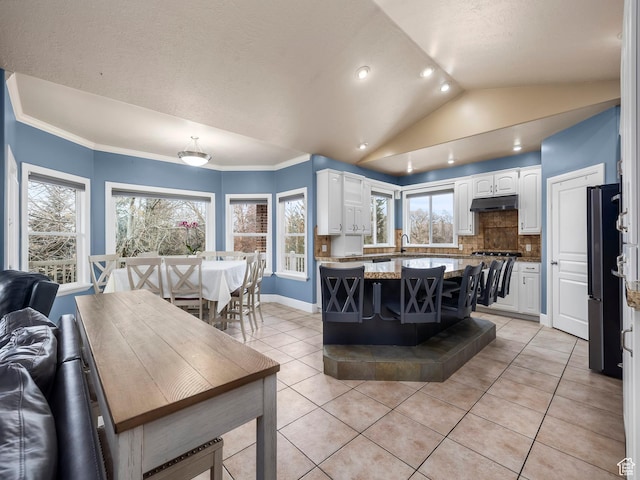 kitchen featuring white cabinetry, refrigerator, backsplash, vaulted ceiling, and light tile patterned floors