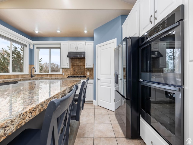 kitchen featuring refrigerator with ice dispenser, double oven, stone countertops, white cabinetry, and decorative backsplash
