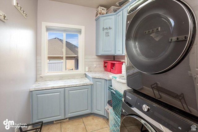 laundry room featuring cabinets, light tile patterned flooring, and stacked washer and clothes dryer
