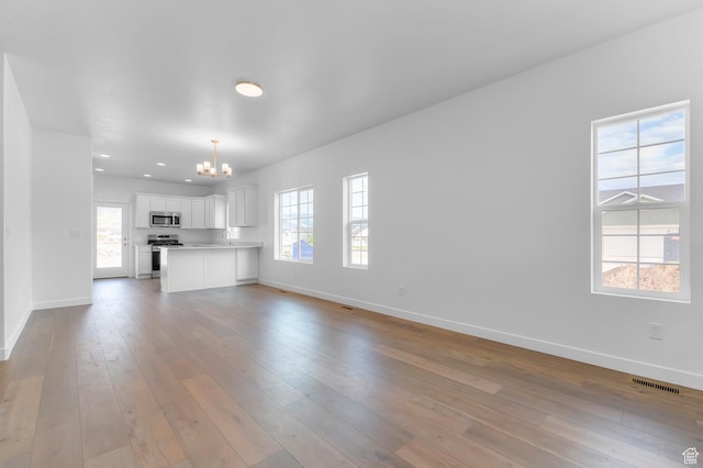 unfurnished living room with a chandelier, baseboards, light wood-type flooring, and recessed lighting
