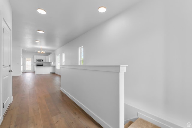 corridor featuring baseboards, light wood-type flooring, and a chandelier