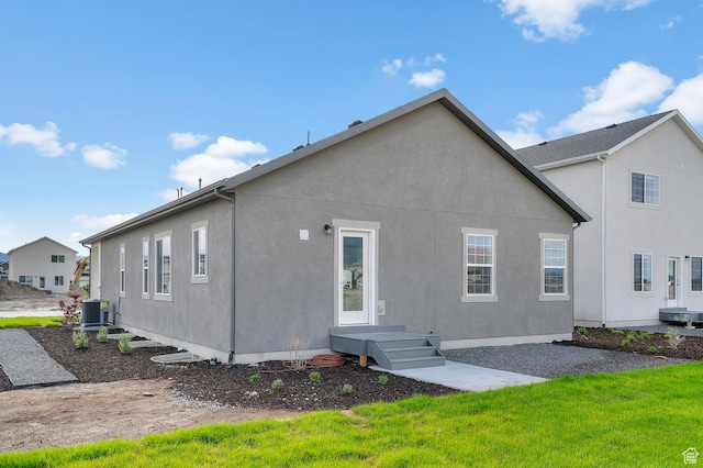 back of house featuring central AC unit, stucco siding, and a yard