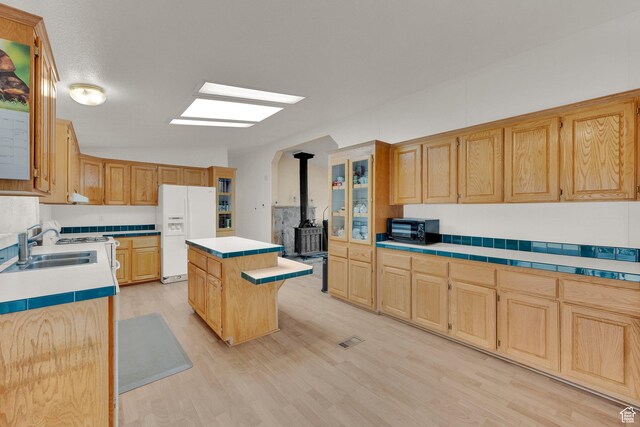 kitchen featuring white fridge with ice dispenser, lofted ceiling, a center island, light wood finished floors, and a wood stove