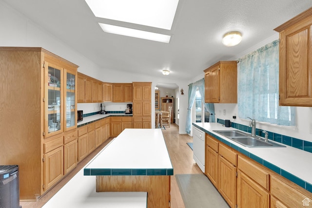 kitchen featuring a sink, dishwasher, arched walkways, light countertops, and glass insert cabinets