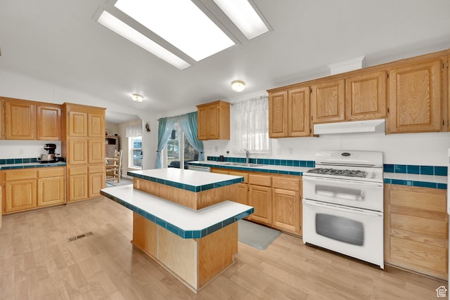 kitchen with double oven range, tile counters, a center island, under cabinet range hood, and vaulted ceiling