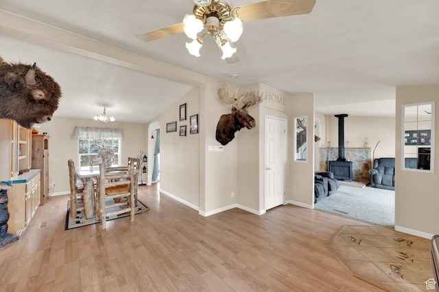 dining room featuring a wood stove, baseboards, light wood finished floors, and ceiling fan with notable chandelier