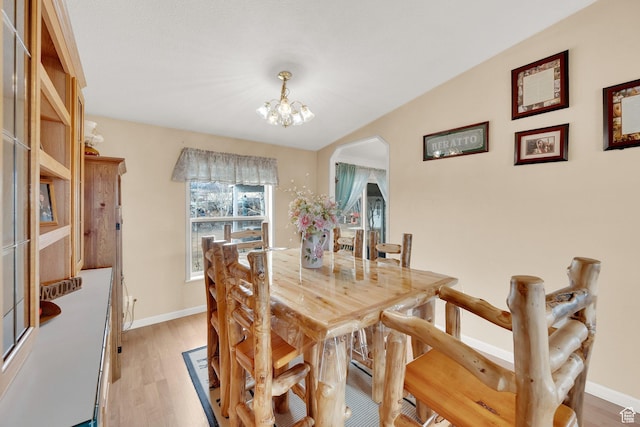 dining room featuring light wood finished floors, baseboards, arched walkways, and a notable chandelier