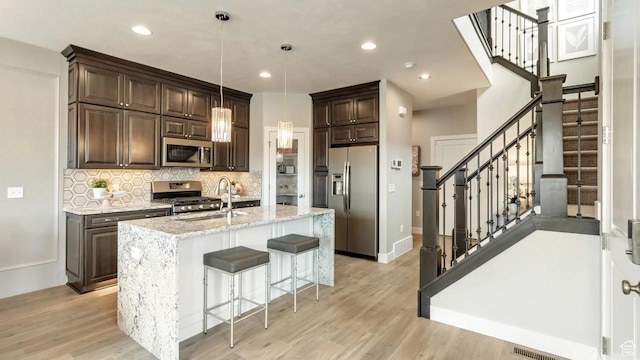 kitchen featuring an island with sink, stainless steel appliances, decorative light fixtures, light stone countertops, and sink