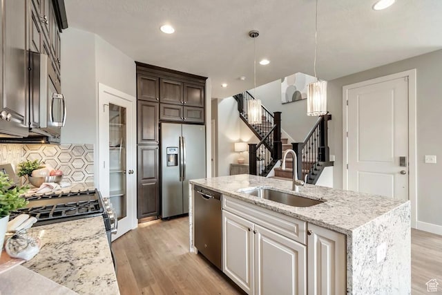 kitchen featuring appliances with stainless steel finishes, dark brown cabinets, an island with sink, light stone countertops, and sink
