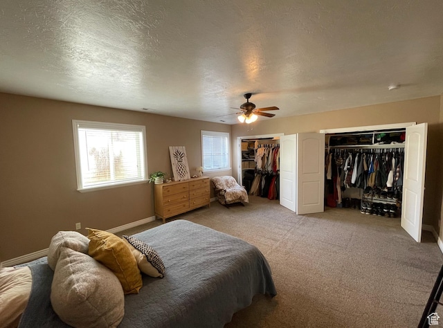 carpeted bedroom with a textured ceiling, ceiling fan, and multiple closets