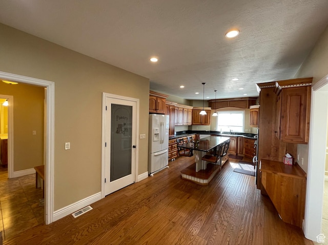 kitchen with a kitchen bar, white fridge with ice dispenser, a center island, pendant lighting, and dark hardwood / wood-style floors