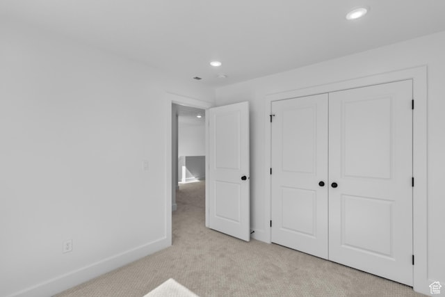 unfurnished bedroom with a closet, recessed lighting, light colored carpet, and baseboards