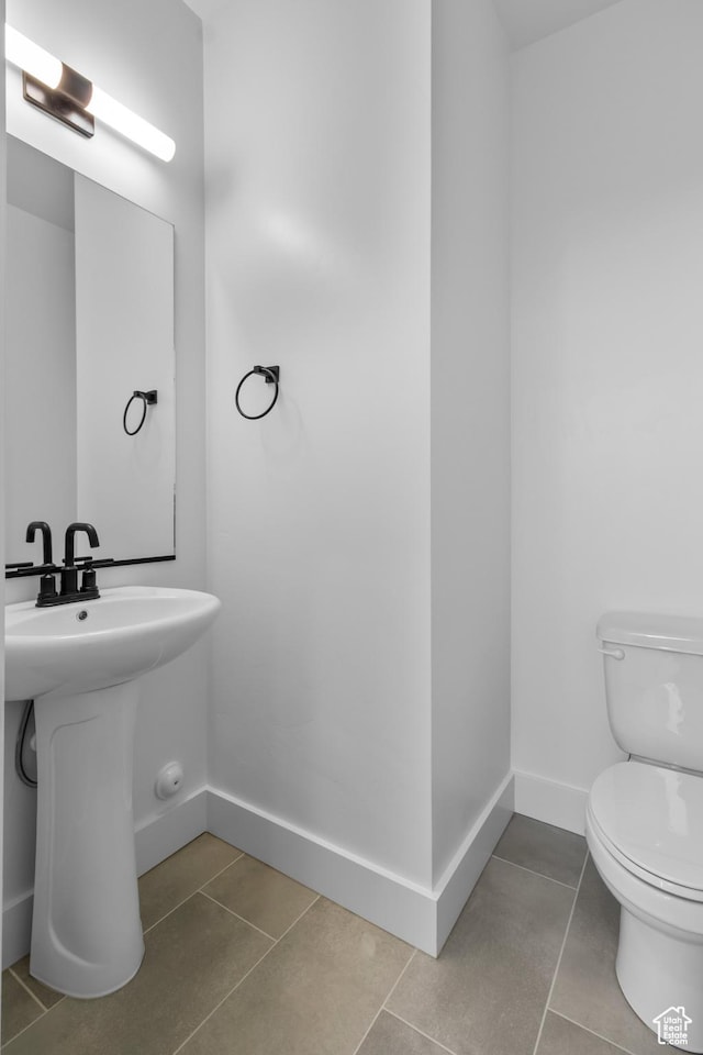 bathroom with tile patterned floors, toilet, baseboards, and a sink