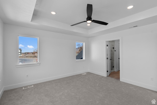 unfurnished bedroom with visible vents, multiple windows, a tray ceiling, and carpet floors