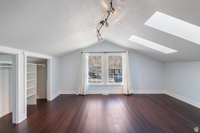additional living space with a textured ceiling, vaulted ceiling with skylight, wood-type flooring, and baseboards