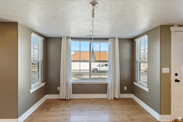 unfurnished dining area with light wood-type flooring, plenty of natural light, a textured ceiling, and baseboards
