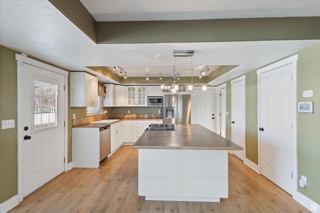 kitchen featuring a center island, stainless steel appliances, light wood-style flooring, white cabinetry, and a sink