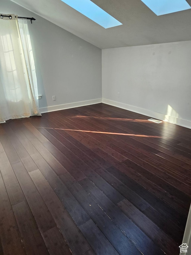 unfurnished room with lofted ceiling with skylight, visible vents, baseboards, and dark wood-style floors