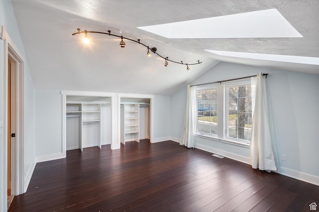 unfurnished bedroom with dark wood-style floors, vaulted ceiling with skylight, baseboards, and two closets