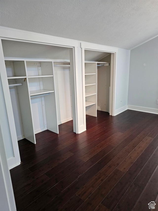 unfurnished bedroom with dark wood-style floors, baseboards, a textured ceiling, and multiple closets