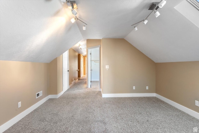 additional living space with carpet floors, lofted ceiling, visible vents, a textured ceiling, and baseboards