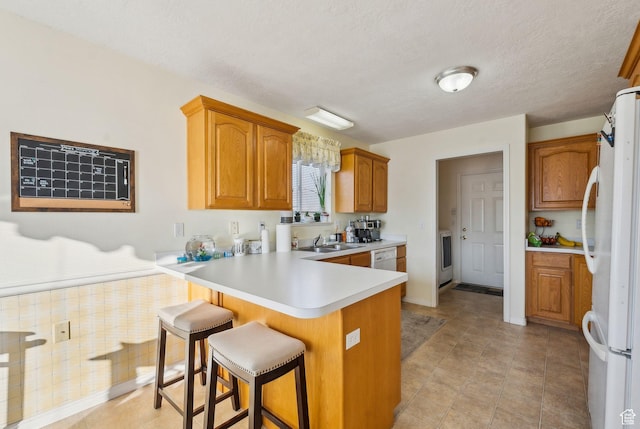 kitchen featuring kitchen peninsula, a breakfast bar, sink, white appliances, and a textured ceiling