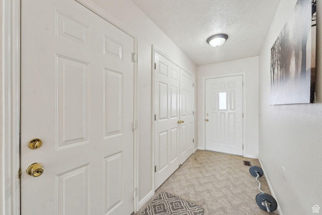 doorway with a textured ceiling and light colored carpet