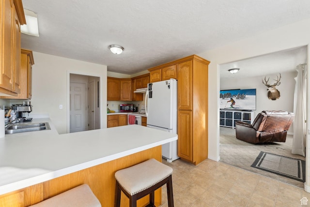kitchen featuring white appliances, sink, a textured ceiling, kitchen peninsula, and a breakfast bar area