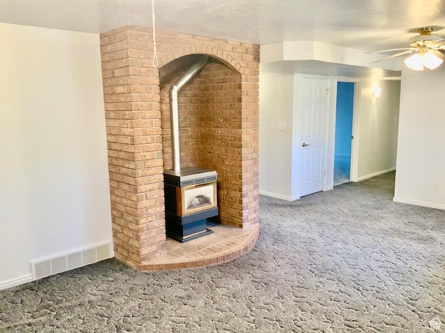 unfurnished living room with a wood stove, ceiling fan, and carpet floors