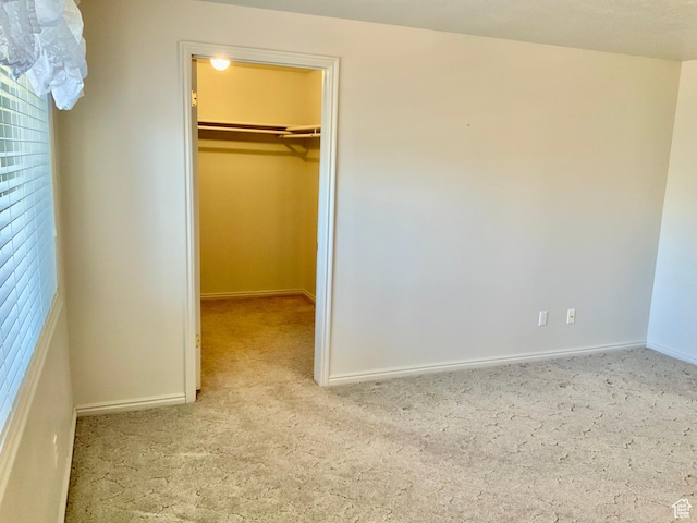 unfurnished bedroom featuring a closet, a walk in closet, and light colored carpet